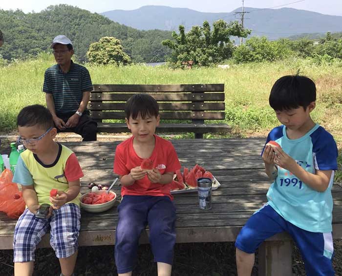 2016년, 마을회관 청소 후 밤만디에 앉아 시원하게 수박을 먹는 아이들. 
